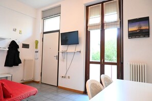 Ein Zimmer mit einem Bett, einem Fernseher, einem Tisch und einem Fenster mit Blick auf Grünflächen.