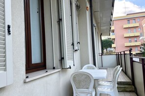 Ein Balkon mit weißem Tisch und Stühlen, ein Fenster mit Rollläden und einem Geländer.