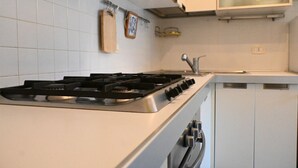 Een keuken met een gasfornuis, witte kastjes en een roestvrijstalen afzuigkap.