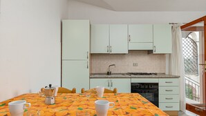 Een keuken met witte kastjes, een betegelde spatwand en een tafel met een tafelkleed met een fruitprint.