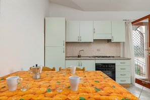 Una cocina con armarios blancos, salpicadero de azulejos y una mesa con mantel estampado de frutas.