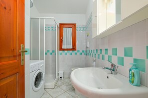 Une salle de bain équipée d’une machine à laver, d’une douche, d’un lavabo et d’une serviette accrochée au mur.