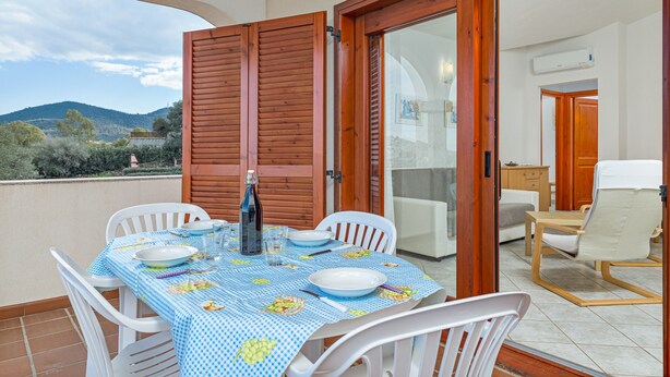 Een balkon met een eettafel, witte stoelen en uitzicht op het landschap.