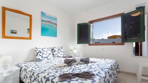 A bedroom with a bed, a bedside table, a mirror, a window, and a painting on the wall.