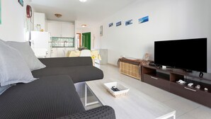 A modern living room with a sofa, a TV, a coffee table, and a kitchen in the background.