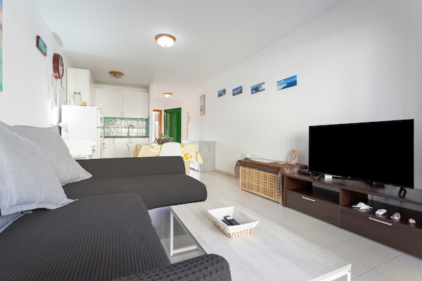 A modern living room with a sofa, a TV, a coffee table, and a kitchen in the background.