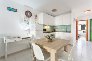 A modern kitchen with white cabinets, a wooden dining table, and white chairs. - Vacation 'La Casita' with Sea View, Shared Terrace and Wi-Fi (Corralejo)