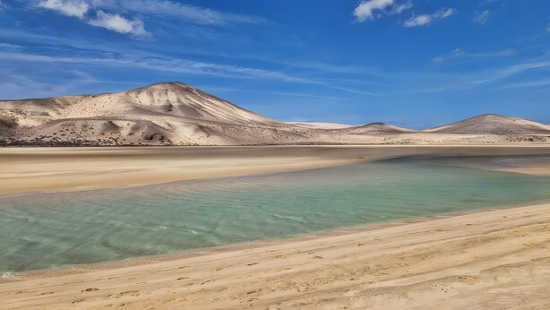 A desert landscape with clear water, sandy beach, and distant mountains.