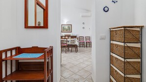 Un couloir avec un banc en bois, un coin repas avec des chaises et une table, et un panier tressé accroché au mur.