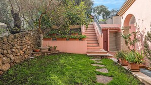 Un mur de pierre, une zone herbeuse, des plantes en pot et un escalier menant à un bâtiment.