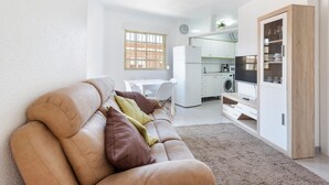 Una sala de estar moderna con sofá, mesa de comedor, zona de cocina y mueble empotrado para la televisión.