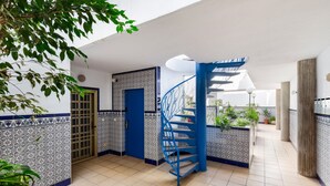 Un pasillo con una escalera espiral azul, paredes de azulejos y plantas en macetas.