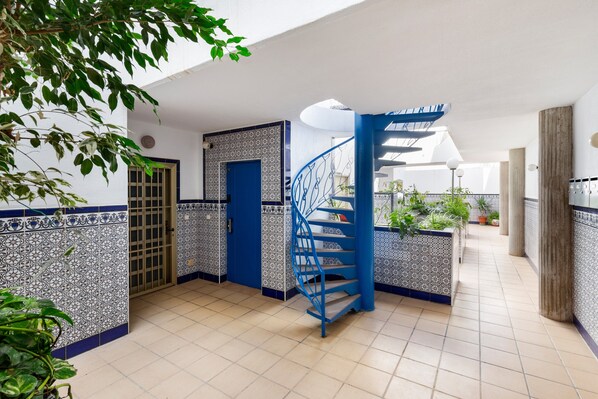 Un pasillo con una escalera espiral azul, paredes de azulejos y plantas en macetas.