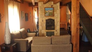 Ein gemütliches Wohnzimmer mit Kamin aus Stein, Holzbalken, einer Couch und einer Treppe.