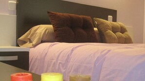 Ein Bett mit Kissen, ein Nachttisch mit Kerzen und ein Lichtschalter an der Wand.