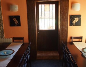 Une pièce dotée d’une porte en bois, de deux appliques murales, d’une table à manger avec des chaises et de deux œuvres d’art encadrées accrochées aux murs.