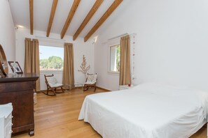 A bedroom with a wooden ceiling, a bed, two rocking chairs, a dresser, and a window with curtains.