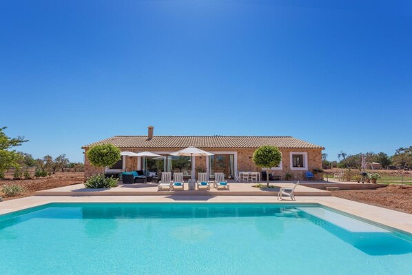 A house with a swimming pool, outdoor seating, and a clear blue sky.