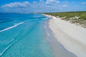 Une plage aux eaux turquoise et limpides, bordée d’un rivage sablonneux.