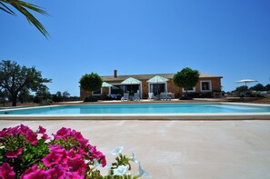 A pool with lounge chairs, a building with a tiled roof, and a clear blue sky.