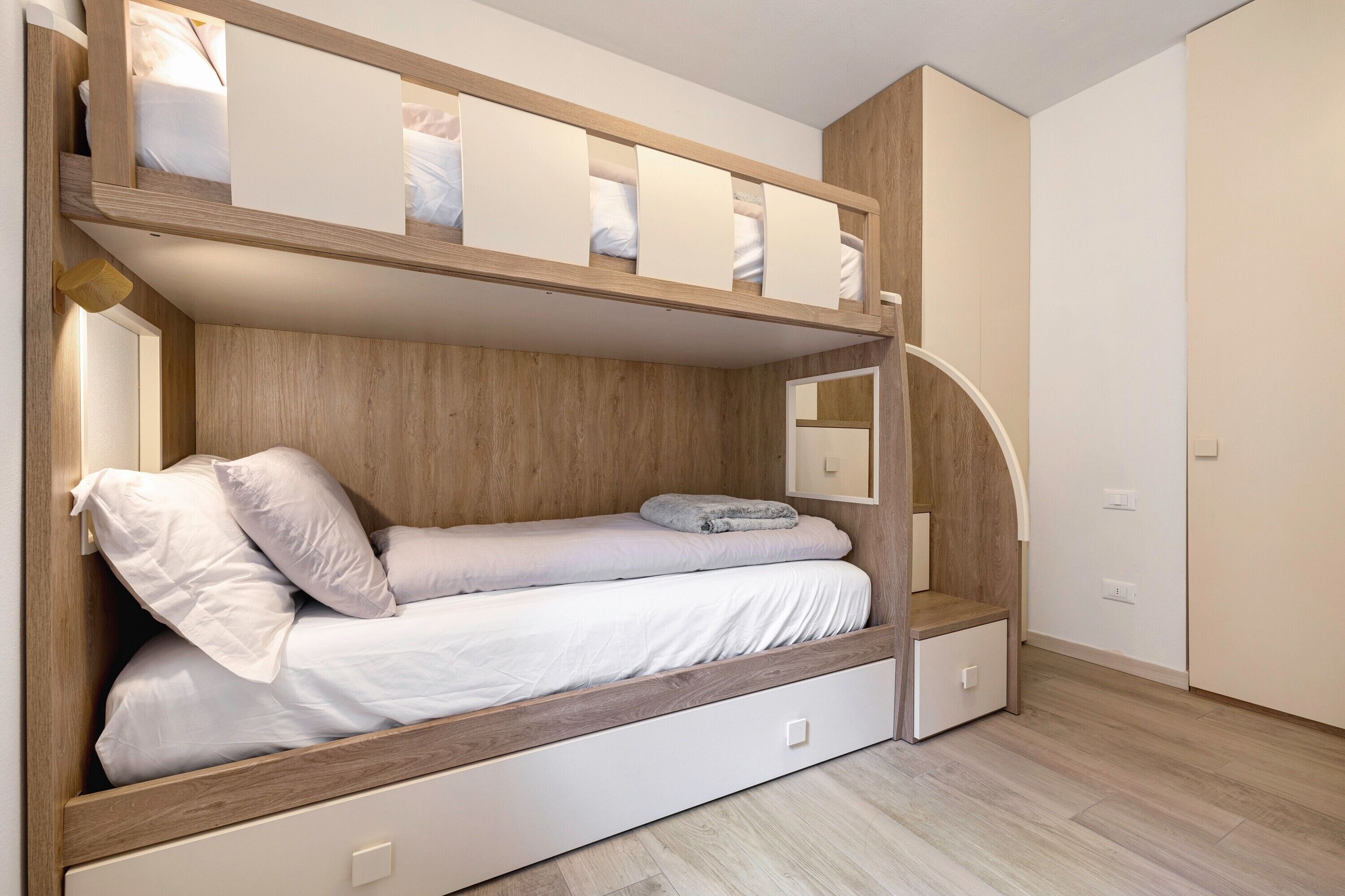 A bunk bed with a wooden headboard, a lower bed with a white mattress, and a small drawer unit.