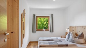 Une chambre à coucher avec un lit en bois, une fenêtre avec des rideaux, une petite table de chevet et une commode.
