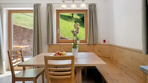 Un coin repas avec une table en bois, des chaises, un vase de fleurs et une vue sur un paysage verdoyant par la fenêtre.