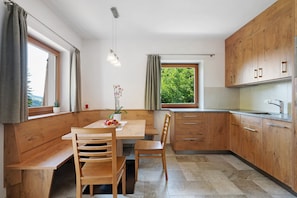 Una cocina moderna con armarios de madera, una mesa de comedor con sillas, una ventana con cortinas y una lámpara colgante.