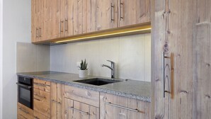 Une cuisine dotée de meubles en bois, d’un plan de travail en granit, d’un évier en acier inoxydable et d’un four encastré.