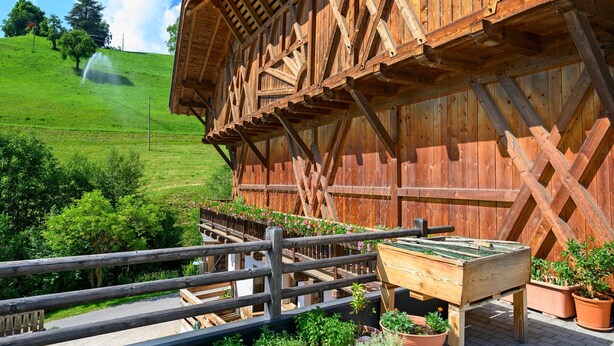 Un bâtiment en bois doté d’un balcon, d’une table en bois et de plantes en pot.