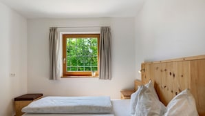 Une chambre avec deux lits, une fenêtre avec des rideaux, une tête de lit en bois et une petite table de chevet.