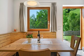 Ein Holztisch mit Flasche und Gläsern, einer Topfpflanze und Blick auf eine grüne Landschaft durch ein Fenster.