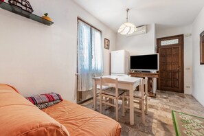 A room with a bed, a table with chairs, a television, a wooden door, and a window with curtains.