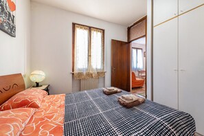 A bedroom with a bed, a bedside lamp, a window with curtains, a wardrobe, and a mirror.