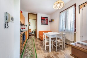 A compact living space with a kitchenette, a dining area with a table and chairs, a patterned rug, and a door leading to another room.