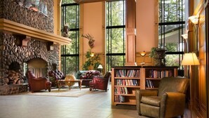 A spacious living room with a stone fireplace, leather furniture, large windows, and a bookshelf.