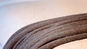 Een detailopname van een structuurrijke stof, mogelijk een deken of kledingstuk, met een vage achtergrond die een huiselijke sfeer oproept.