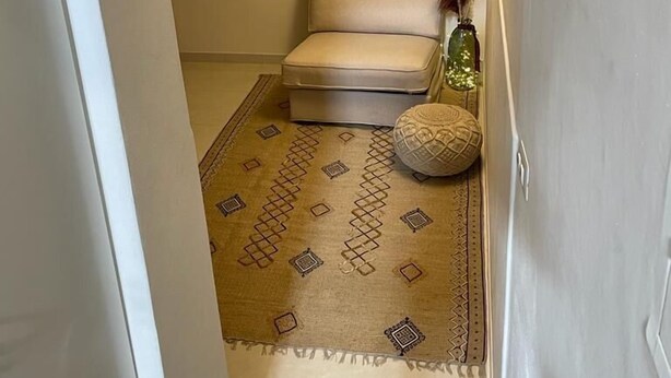 Un pasillo estrecho con un sofá color beige, una alfombra estampada y un pequeño jarrón decorativo.