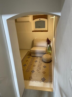 Un couloir étroit avec un canapé beige, un tapis à motifs et un petit vase décoratif.