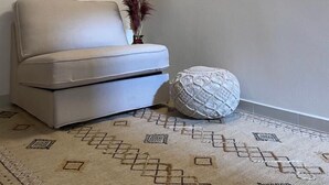 Una sala moderna con un sofá blanco, un tapete estampado y una pequeña planta decorativa.