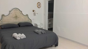 Una cama bien hecha con ropa oscura, dos almohadas y dos toallas enrolladas.