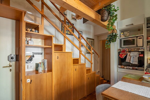 A wooden staircase with built-in shelving, a kitchen area with appliances, and a hanging plant.