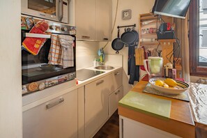 A compact kitchen with a stove, oven, and a sink. There are hanging pots and a bowl of lemons on the counter.