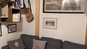 A living room with a grey sofa, a wooden guitar, and framed pictures on the wall. - Small and cozy studio apartment in Florence (Florence)