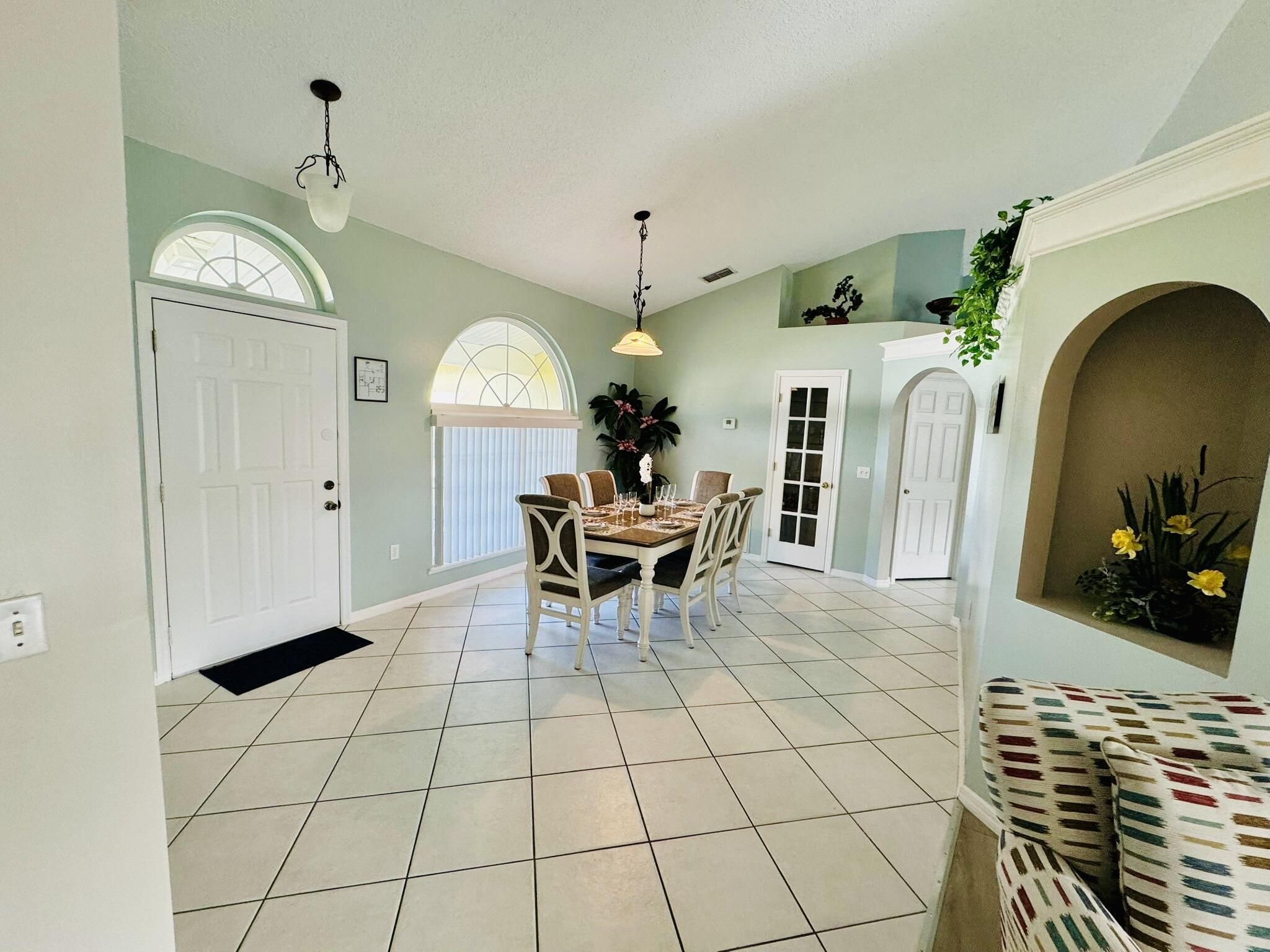 A spacious dining area with a large table and chairs, a chandelier, and a door leading to another room.