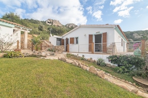 A white building with a stone pathway, a small garden, and a mountainous backdrop.