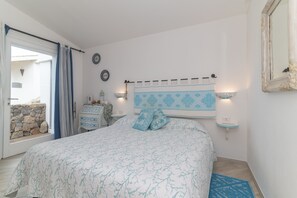 A bedroom with a bed, a bedside table, a nightstand, a wall-mounted light, a mirror, and a view of the outside. - Guest House 'Barbagia Plus' with Mountain View, Wi-Fi and Air Conditioning (Palau)
