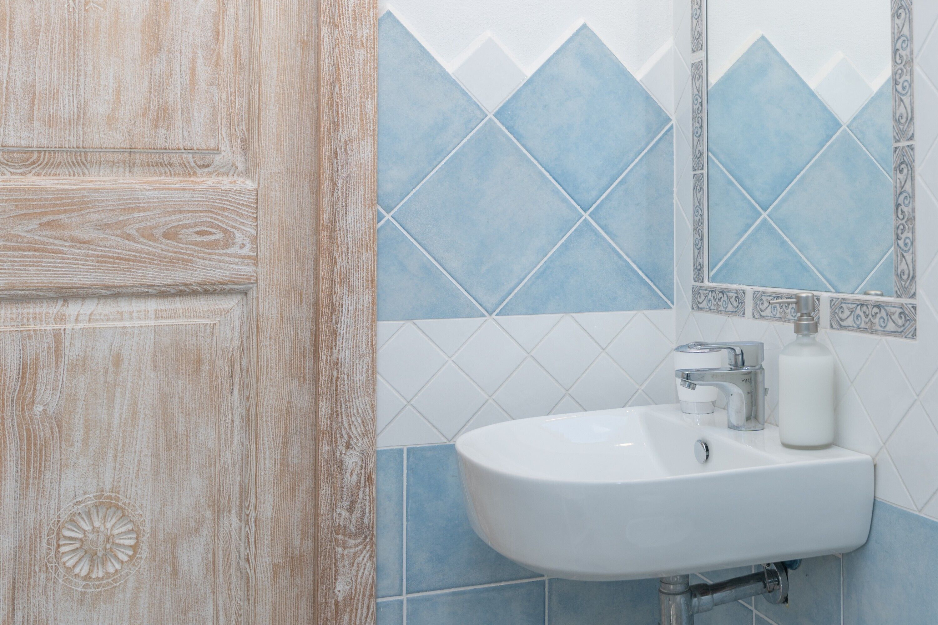 Ein Badezimmer mit Holztür, weißem Waschbecken und blauen Fliesen mit Rautenmuster.