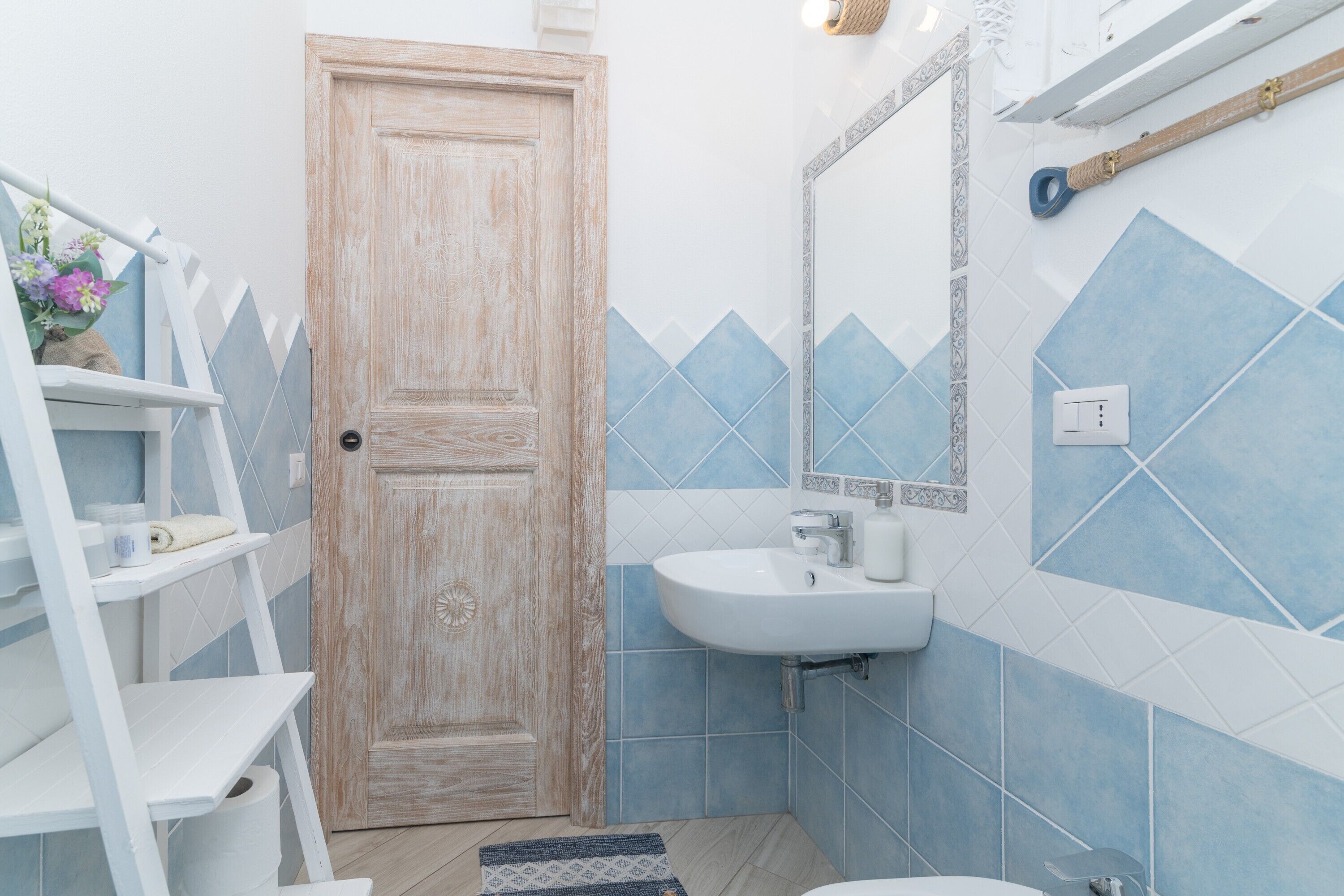 A bathroom with a wooden door, white shelves, a sink, and blue-tiled walls.