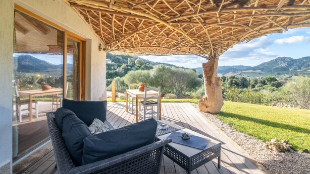 Un espace extérieur aménagé avec des meubles en osier, une table avec une théière et une vue sur la campagne.